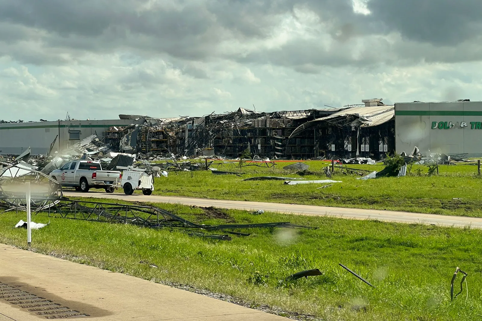 The ruins of a destroyed Dollar Tree warehouse sits on a grass lawn.