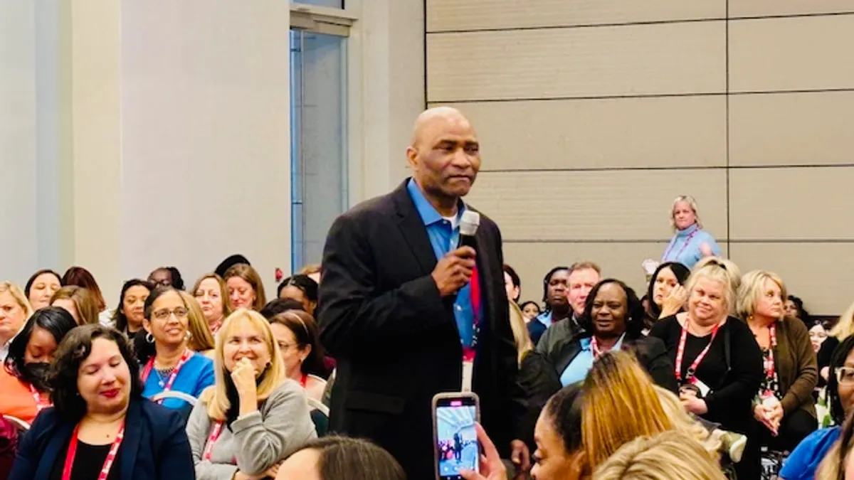 Person is standing with a microphone in a roomful of people sitting in chairs in rows.