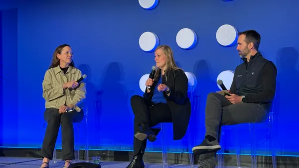Three people sit on a conference stage.