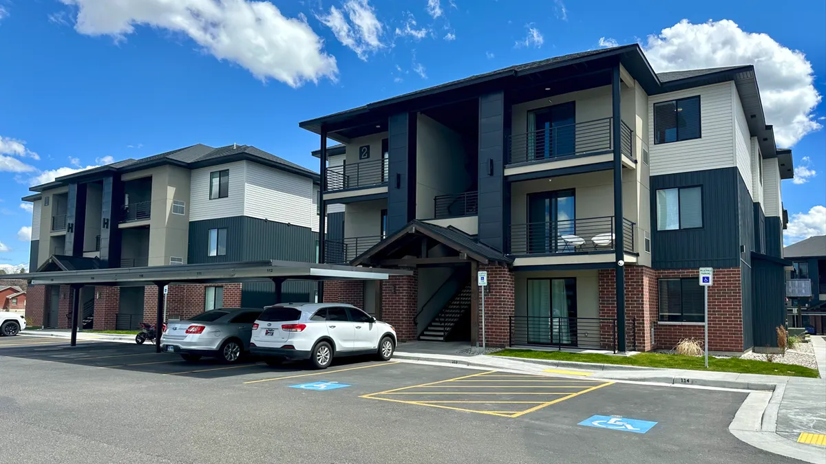 Three-level apartment building with cars and parking lot in the foreground.