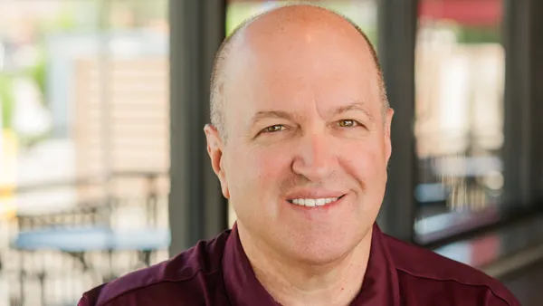 A smiling white man in a burgundy Noodles & Company shirt.