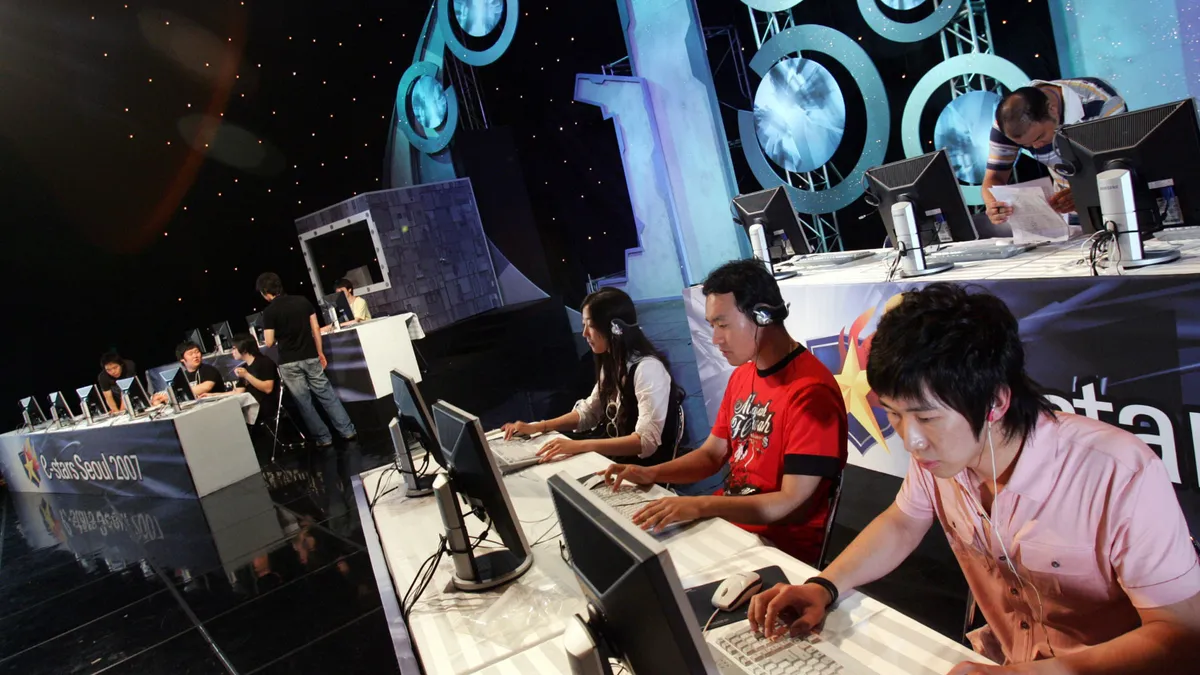 A group of people sit in front of computer monitors at an esports event.