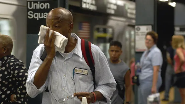A person wipes their face surrounded by a crowd on a subway platform.