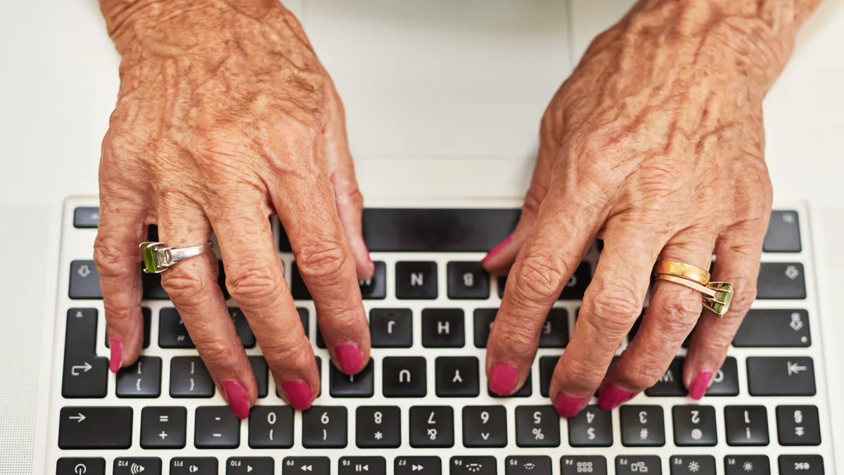 Cropped shot of wrinkled hands, with nail polish and a wedding ring, typing on a laptop keyboard