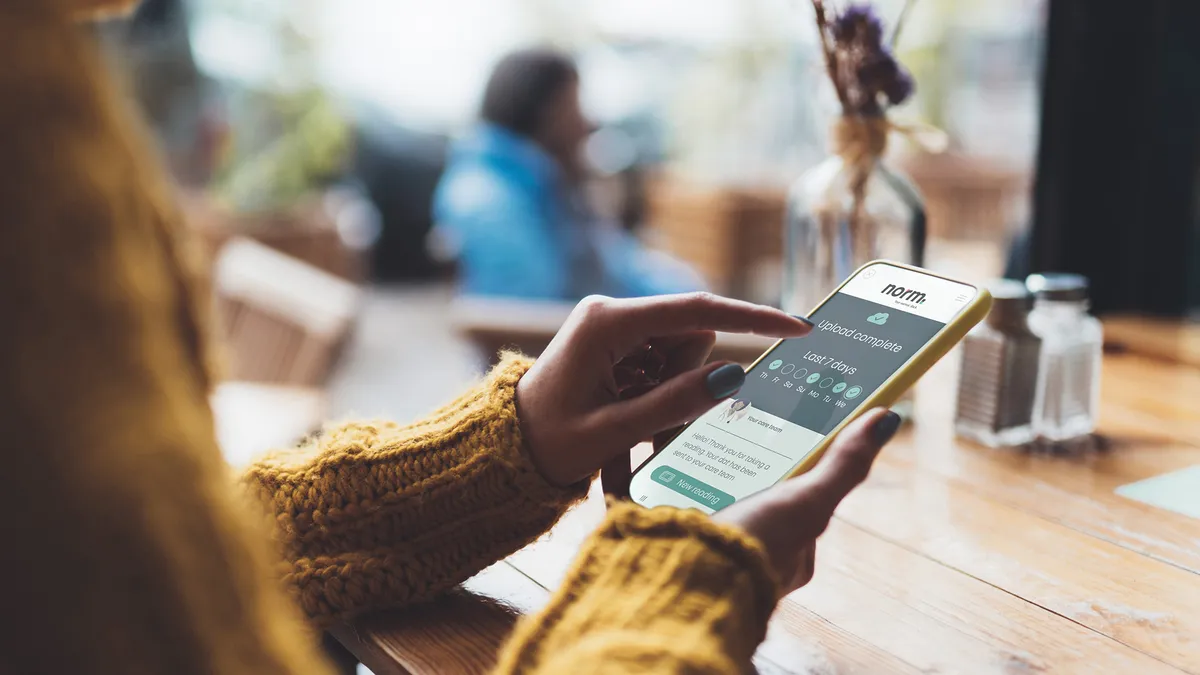 A picture of a person in a dark yellow seater holding their smartphone and looking at their health data.