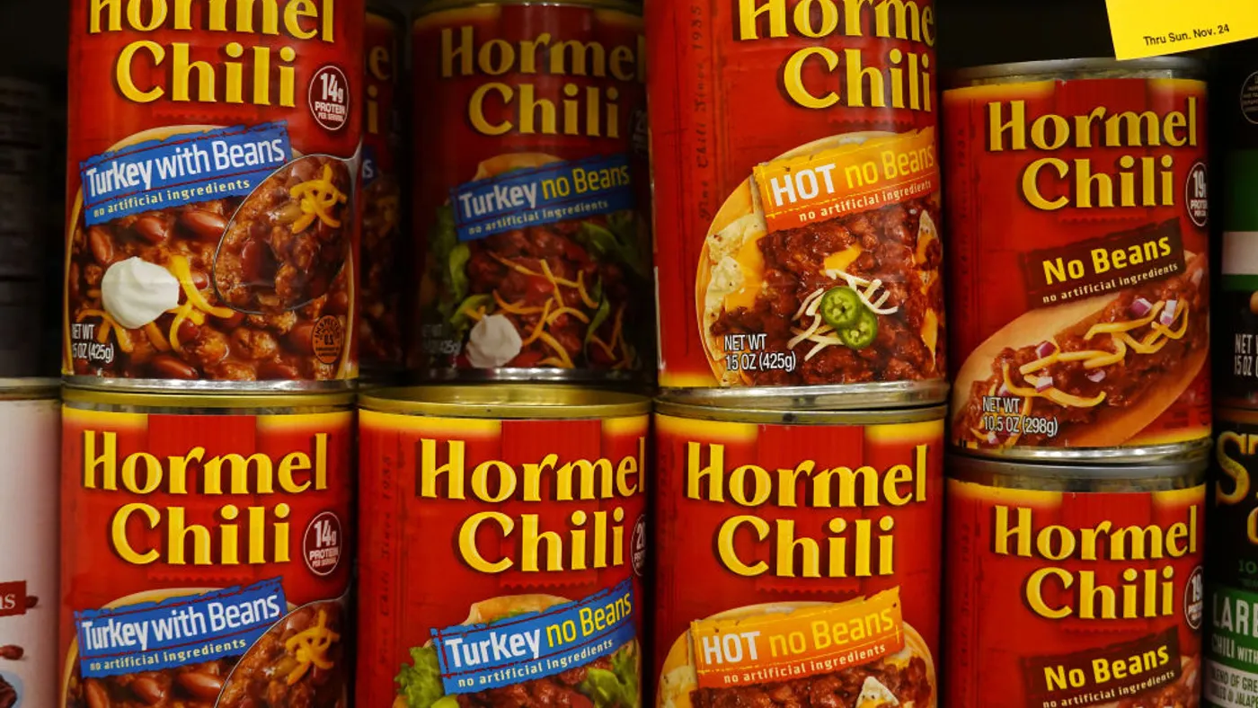 Cans of Hormel chili are displayed on a shelf.