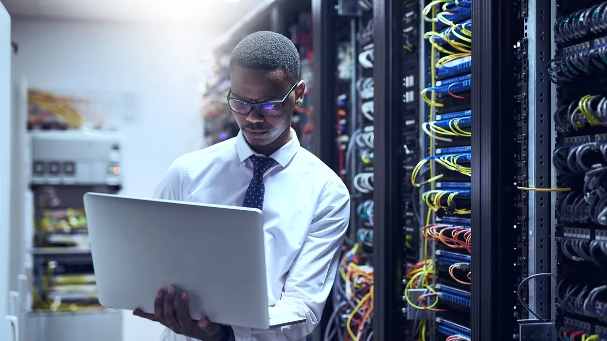 Cropped shot of a IT technician working on his laptop while standing inside of a server room.