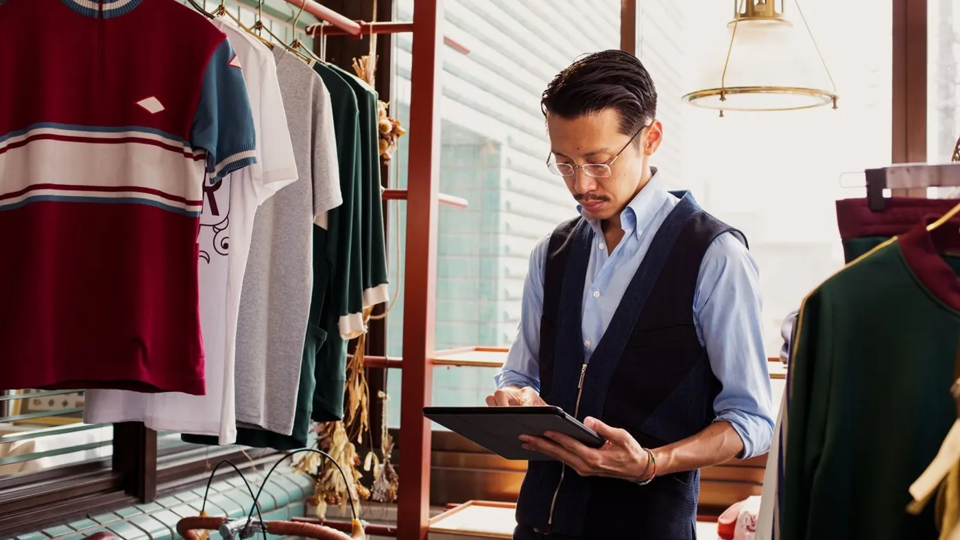 Salesman standing in clothing store, looking at digital tablet.