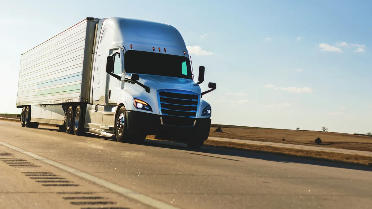 A tractor-trailer on an interstate at dusk.