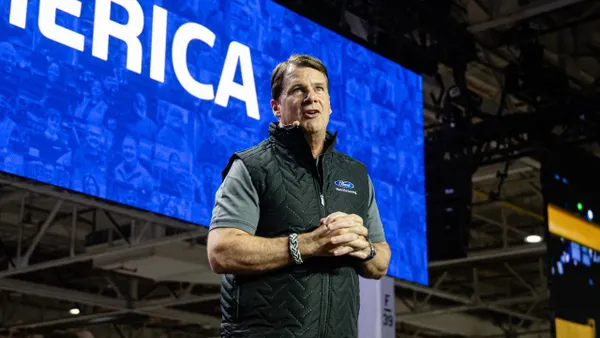 Ford CEO Jim Farley speaking to workers at the automaker's Kentucky Truck Plant in April 2025 with a large blue display screen behind him.