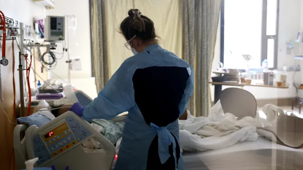 A nurse stands over a patient's bedside in a hospital.