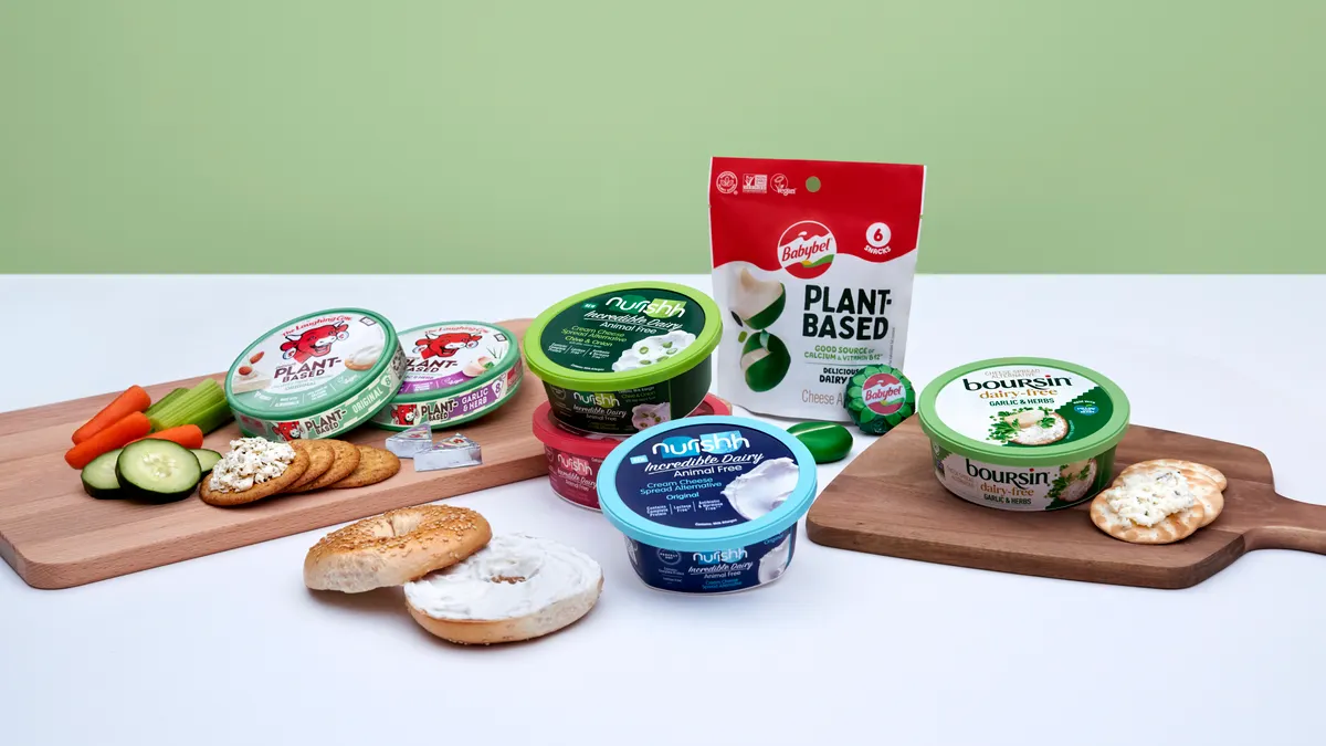 Packages of several of Bel Brands' plant-based and alternative dairy options on and near wooden cutting boards with crackers, cut vegetables and a bagel nearby.