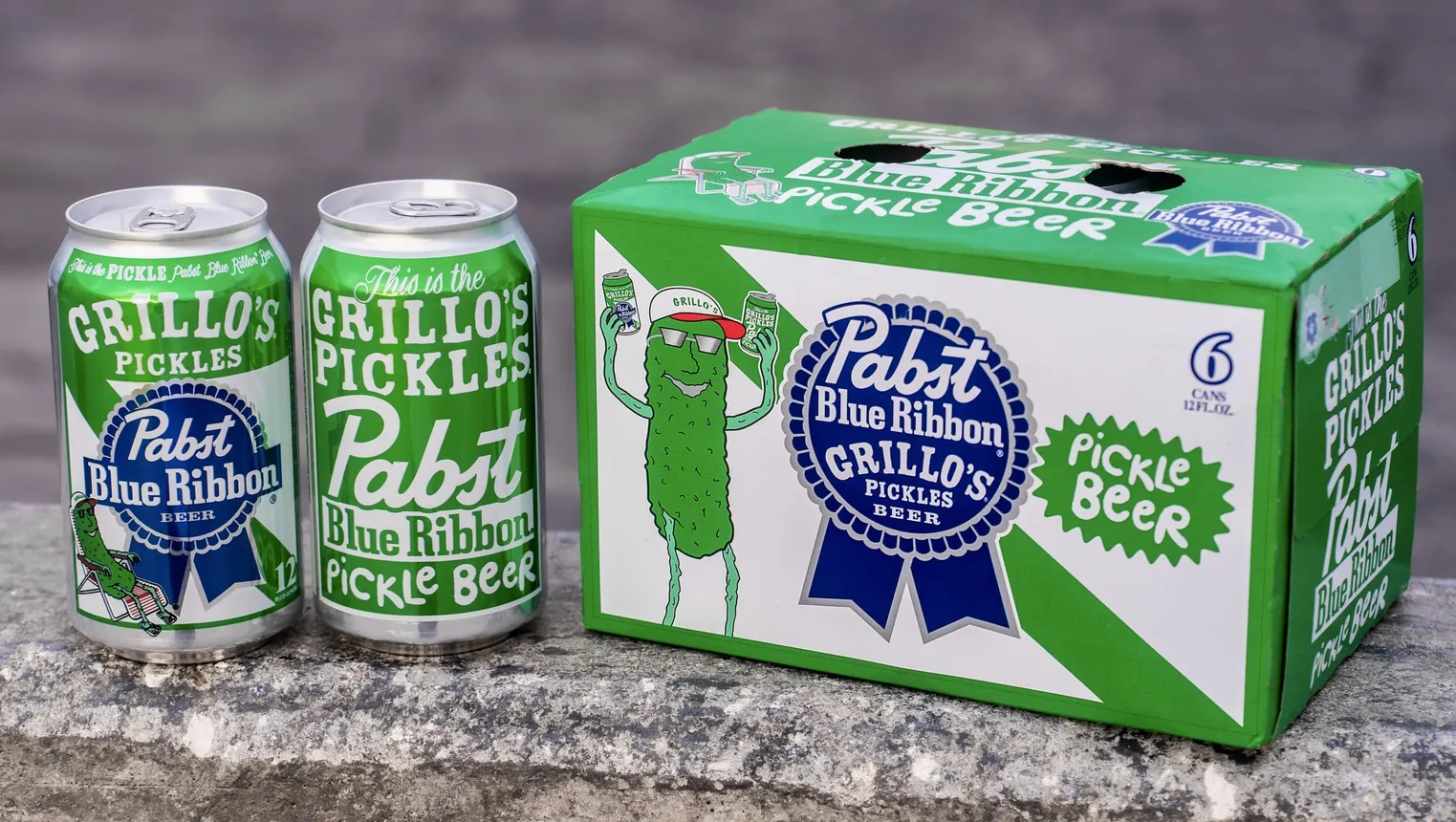 Two cans of Pabst/Grillos beer are pictured next to a box of them.
