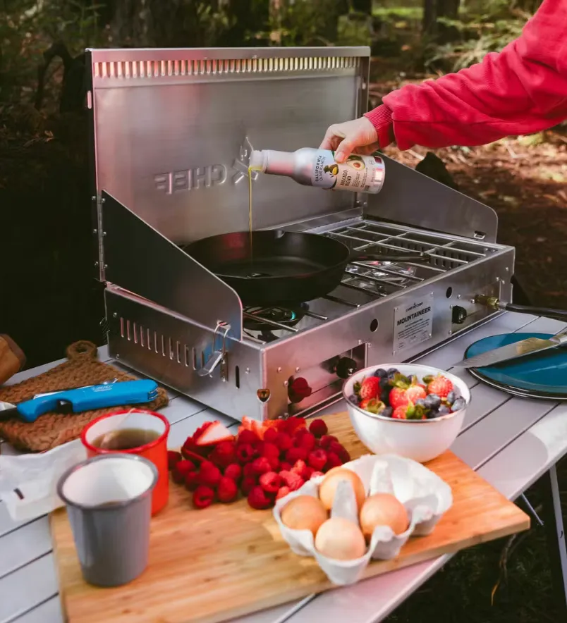 Person pouring olive oil into pan on outdoor grill