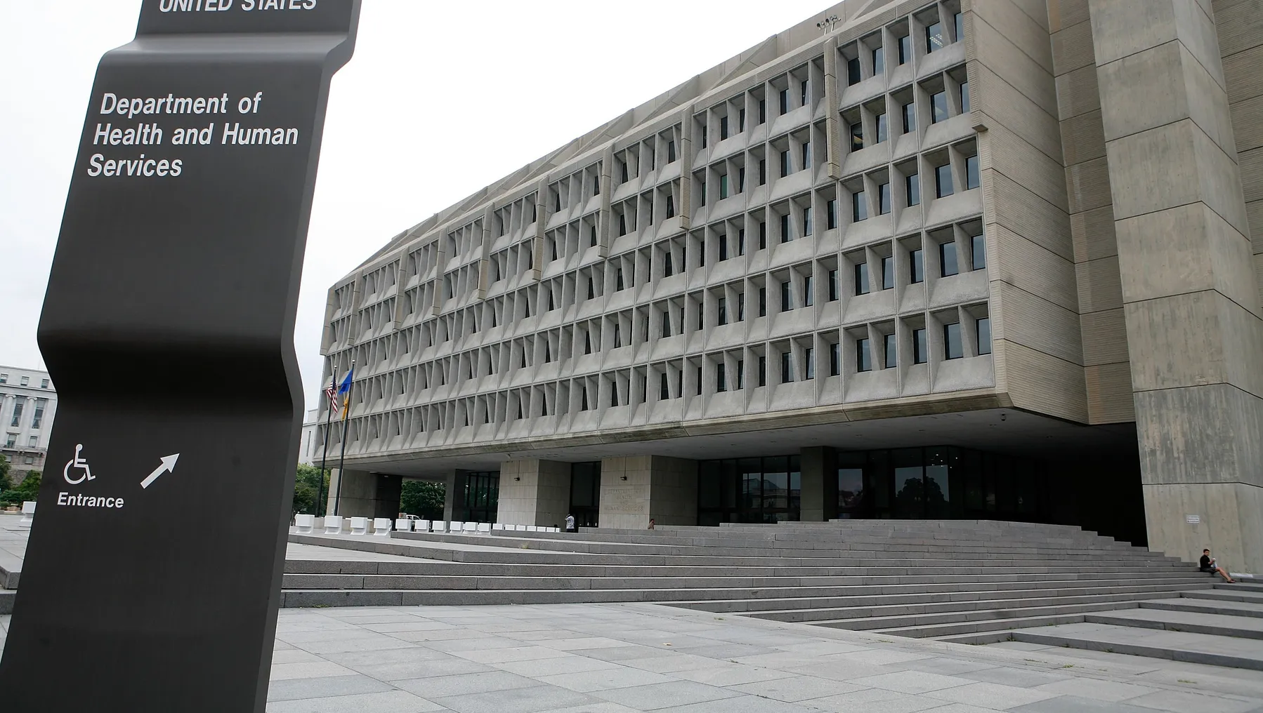 A picture of the exterior of the US Department of Health and Human Services. In front of the building is a black sign designating the building's name.