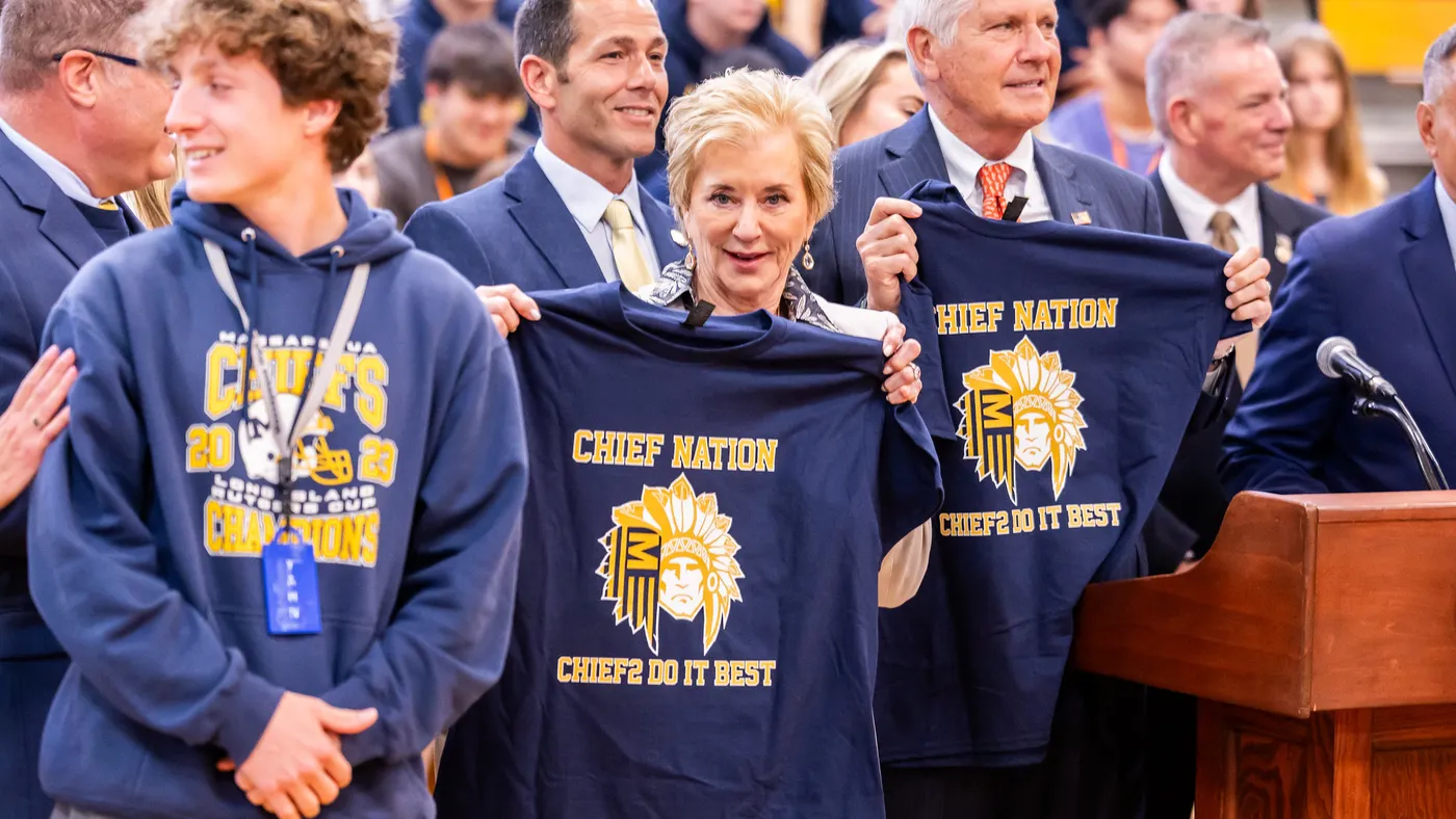 Linda McMahon stands with a T-shirt in her hands featuring a Native American mascot