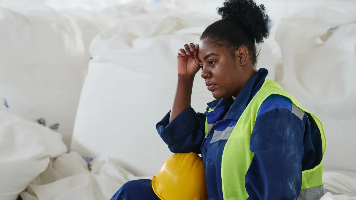 Young tired female engineer or worker of warehouse sitting by heap of huge white sacks with raw materials