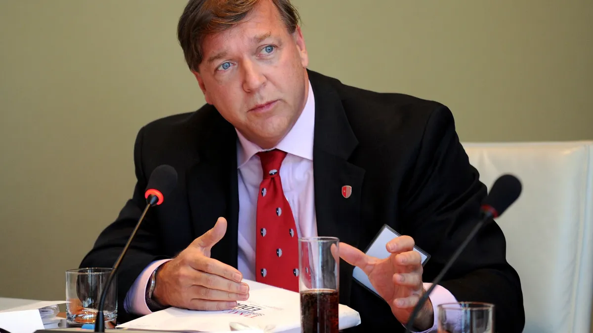 A close-up of a white man speaking into a panel microphone.