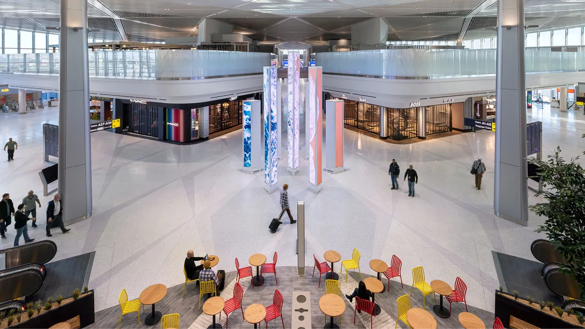 Aerial view of a concessions area with shops and red and yellow chairs around red tables, with gates in the background.