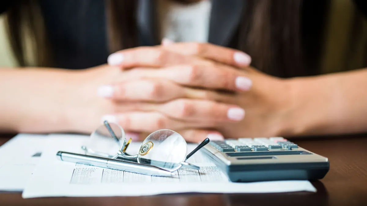 Close up of businesswoman's hands with pen, glasses, and calculator doing some financial calculations