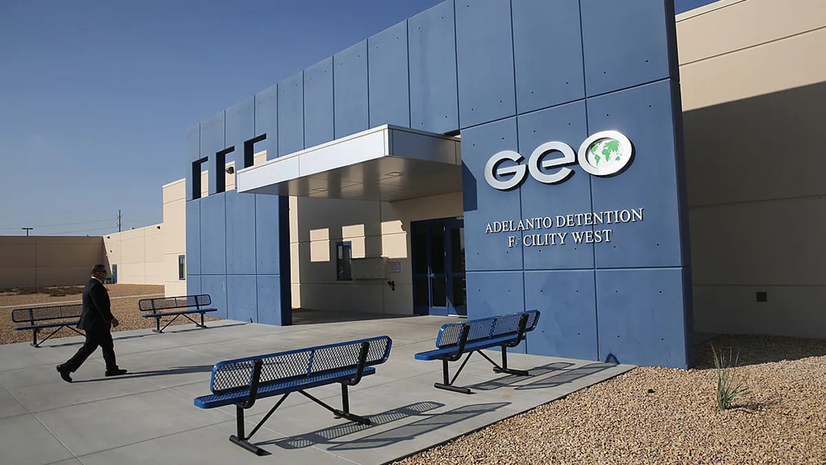 A businessperson walks past metal benches toward the entrance of a detention facility owned by Geo Group.