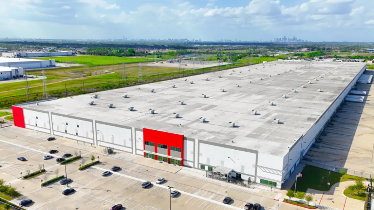 A large warehouse building with cars parked in front of it is shown.