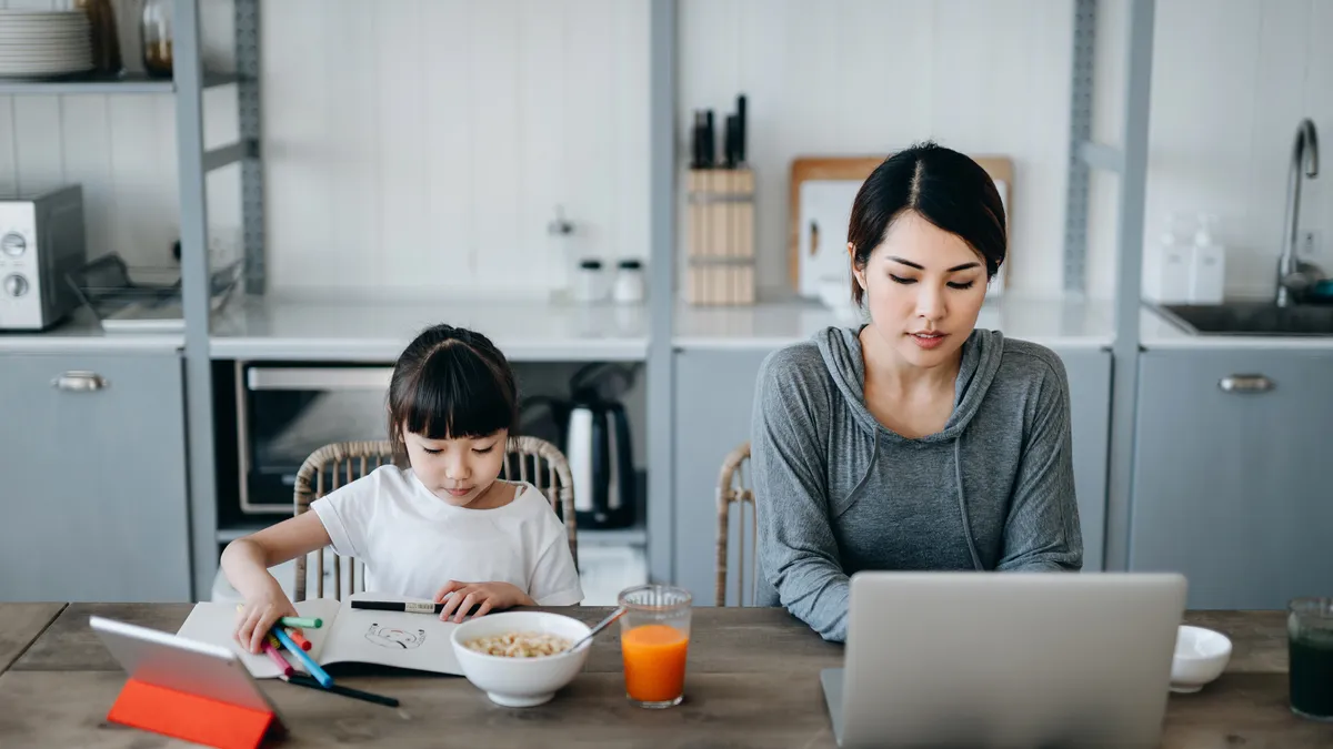 Person working from home on a laptop while daughter is drawing beside her