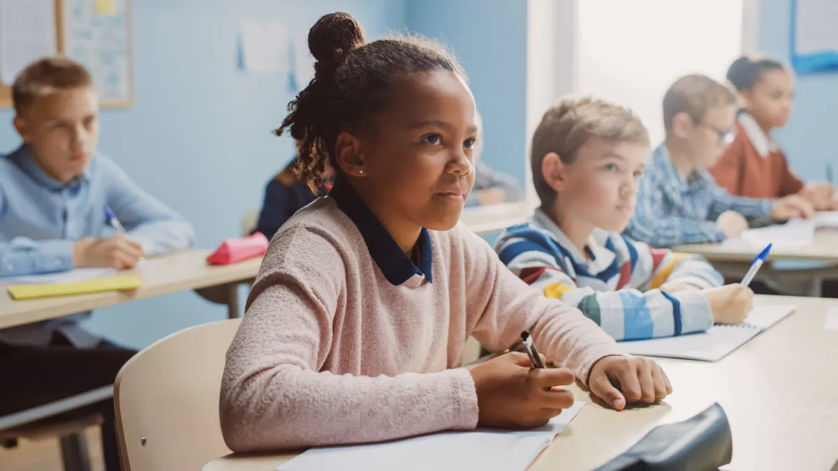 A student at a school desk looking up smiling and writing in their workbook