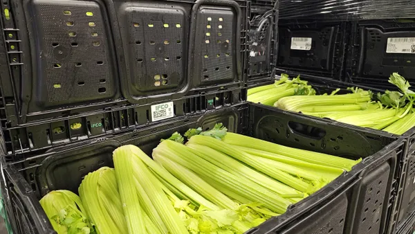 Two black reusable containers in a warehouse holding celery