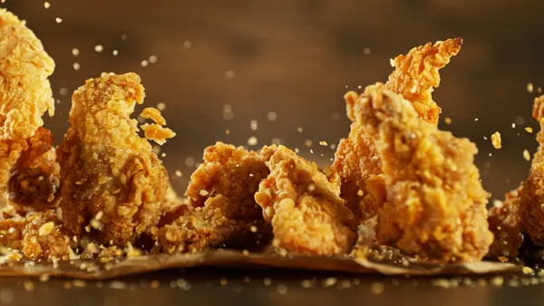A photo of fried chicken falling to a wooden surface with a paper on top.