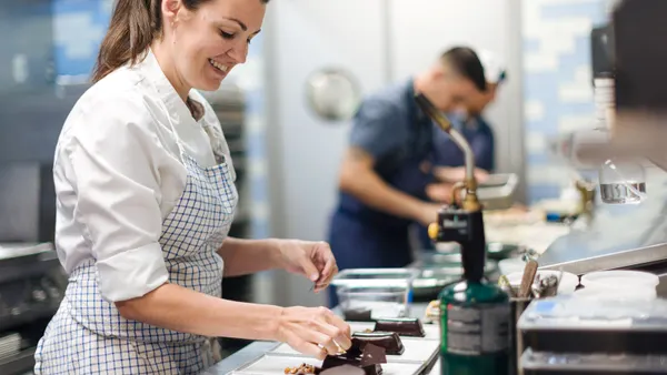 A person stands over dishes of chocolate dessert inside a restaurant kitchen.