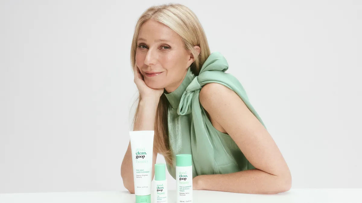 Celebrity Gwyneth Paltrow wearing a light blue shirt posed in front of three white product bottles