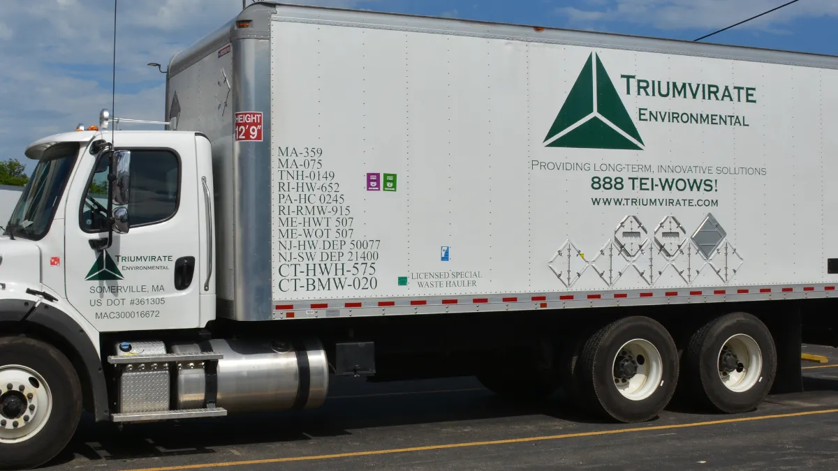 Side view of a white box truck with the Triumvirate Environmental logo