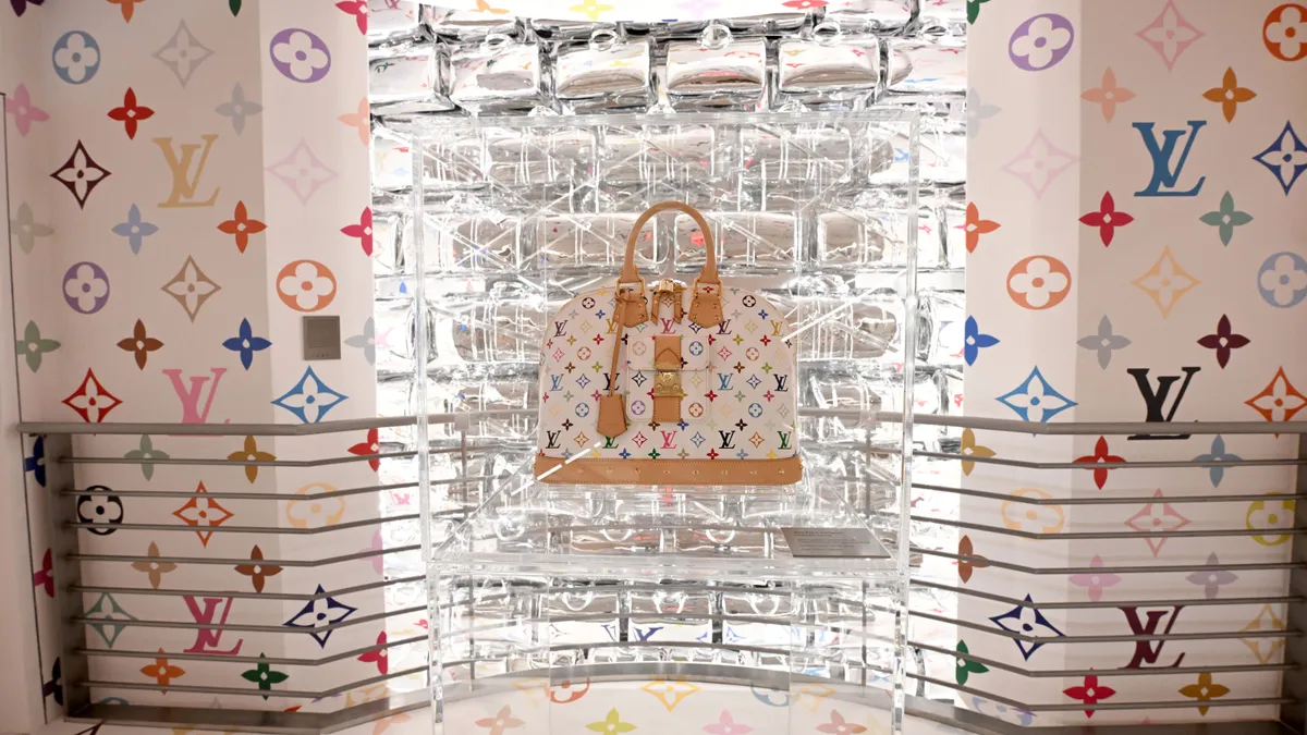 A colorful Louis Vuitton handbag sits in a clear display case.