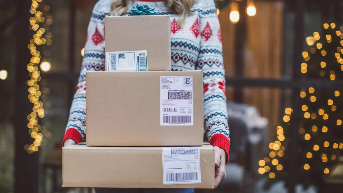 Mature women celebrating Christmas alone during hers coronavirus self-isolation period. She is standing on porch and holding gifts.