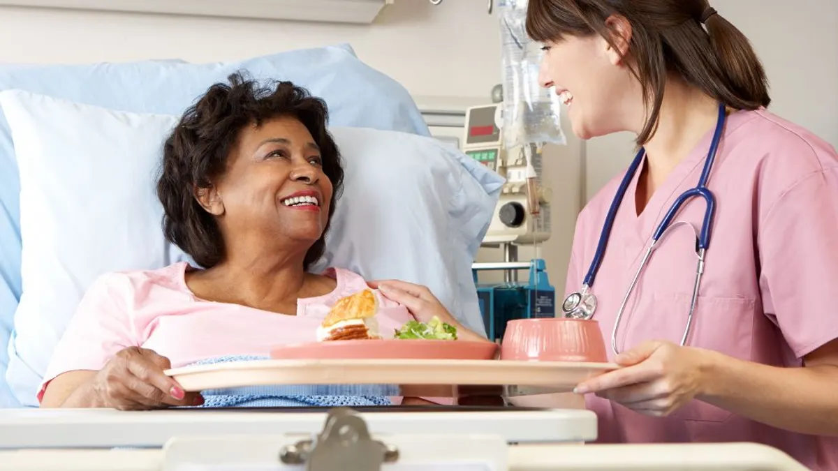 Patient smiling at nurse deliver meal in a hospital room.