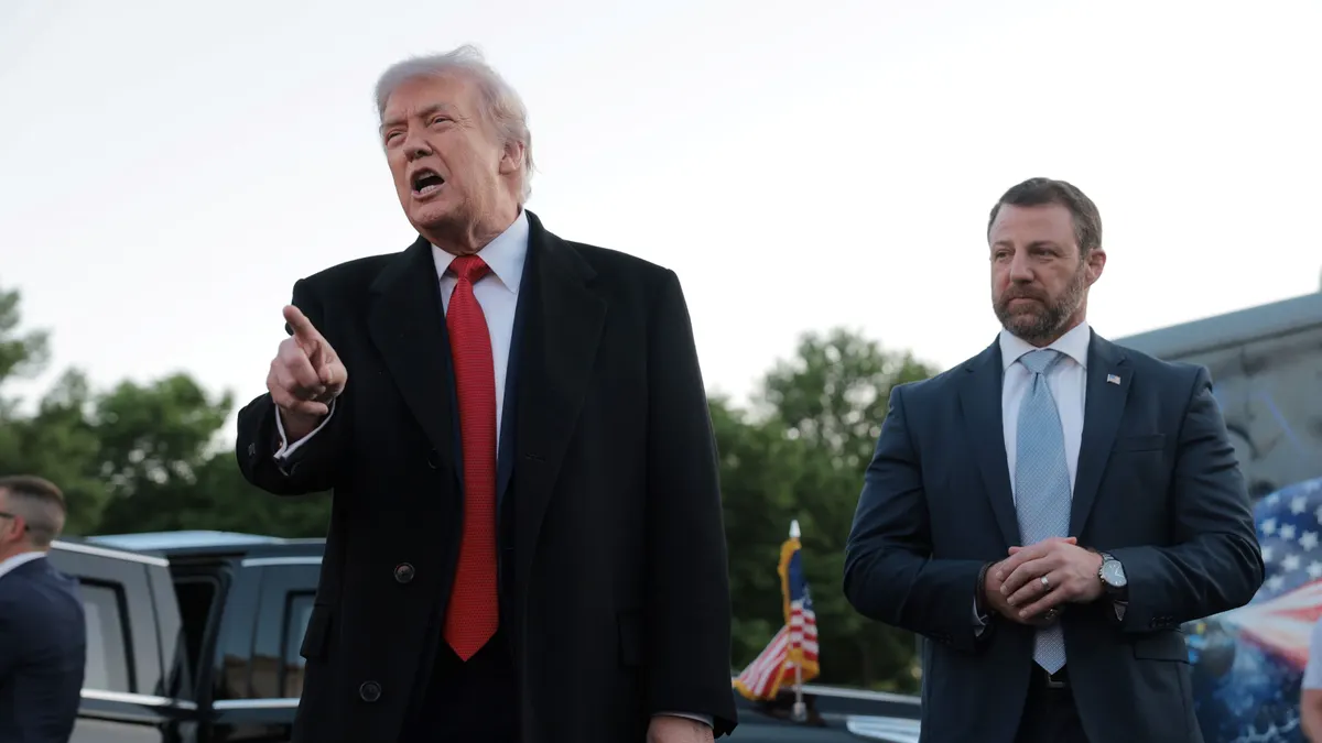 U.S. President Donald Trump speaks to reporters while pointing and standing next to U.S. Secretary of Homeland Security Markwayne Mullin in front of a line of cars.