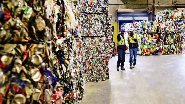 workers walk by bales of aluminum cans at a recycling facility