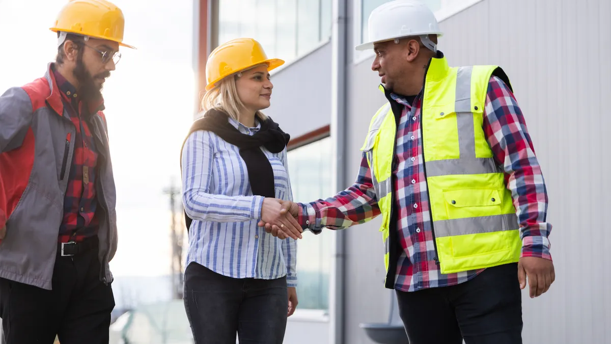 Three people standing, shaking hands wearing construction hats and jackets