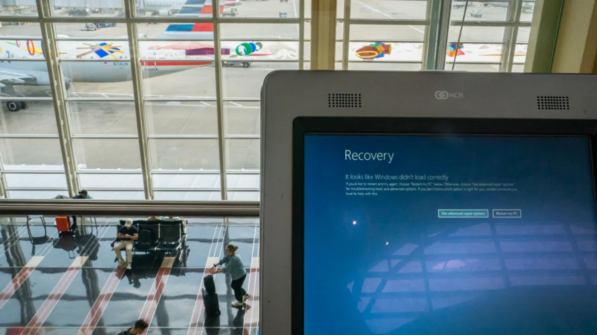 A computer in the foreground shows a blue screen with the words "recovery," and in the background people with suitcases walk by in front of large windows overlooking an airport tarmac.