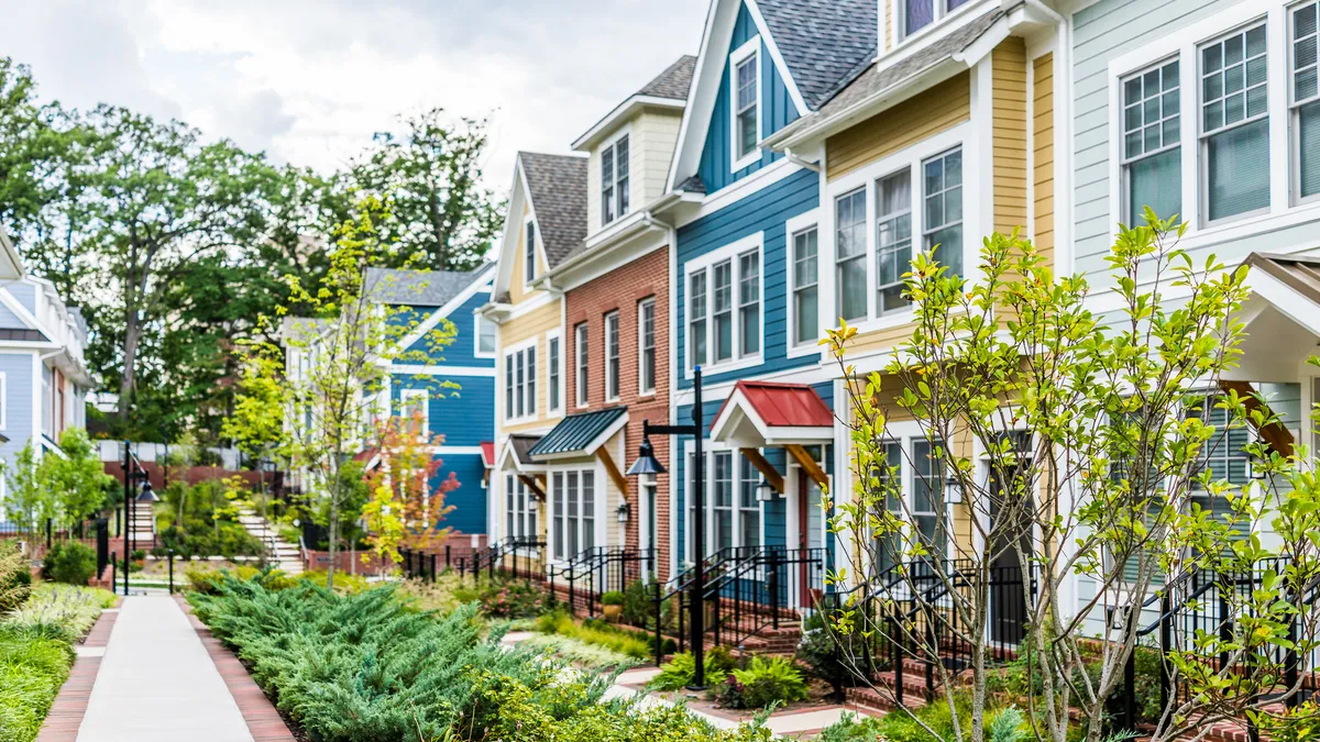 Row of colorful, red, yellow, blue, white, green painted residential townhouses, homes, houses with brick patio gardens in summer.