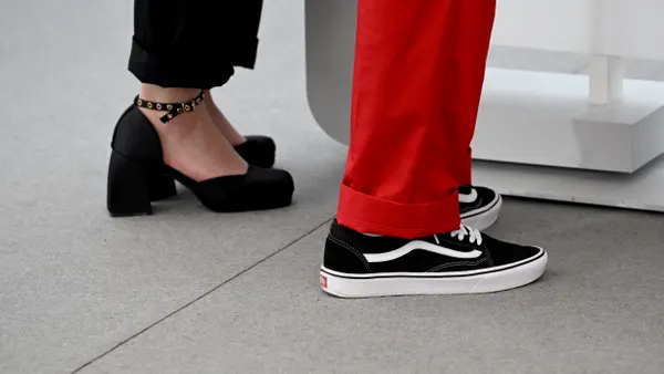 A close up of two people's shoes, one wearing heels, then other Vans.