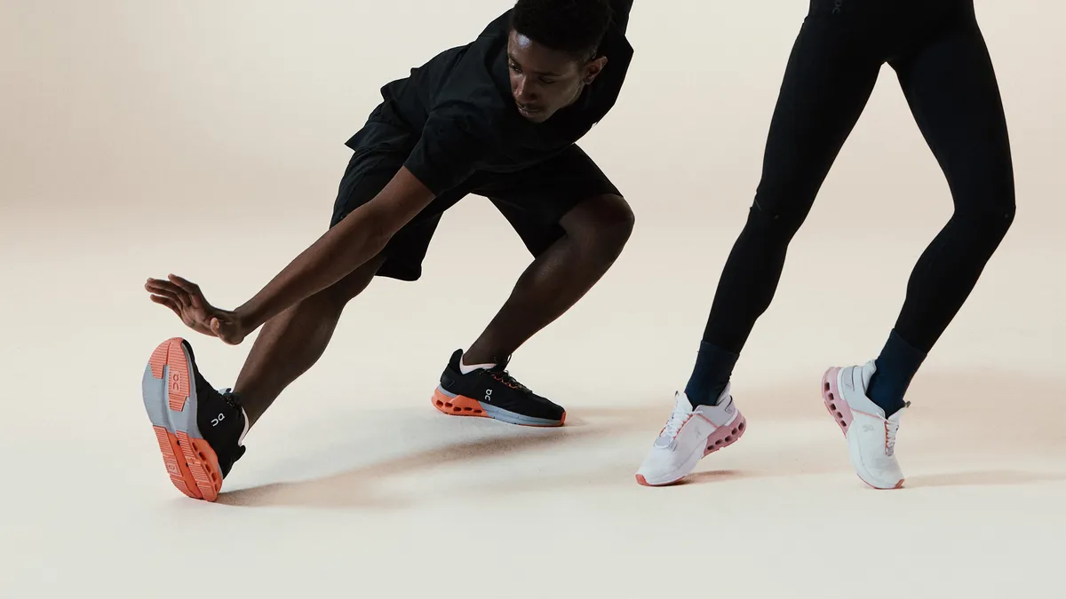 Two models wearing black athletic clothing stretch while wearing colorful sneakers