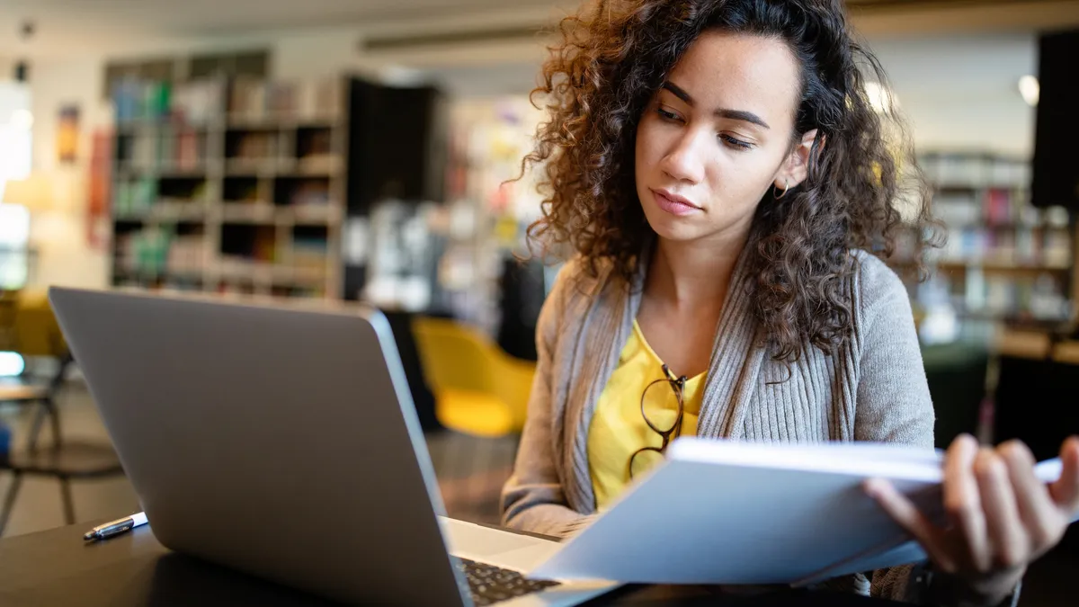 Young afro american woman sitting at table with books and laptop for finding information - stock photo