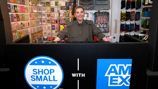 Person stands in small store behind counter with American Express signage.