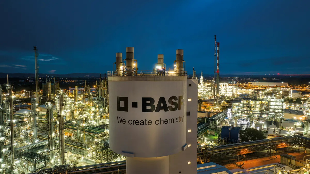 A white tower with the black BASF logo on it, surrounded by a lit facility at night.