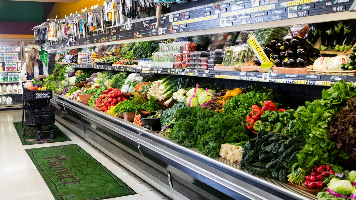 Person with a cart shopping in a grocery store's produce section.