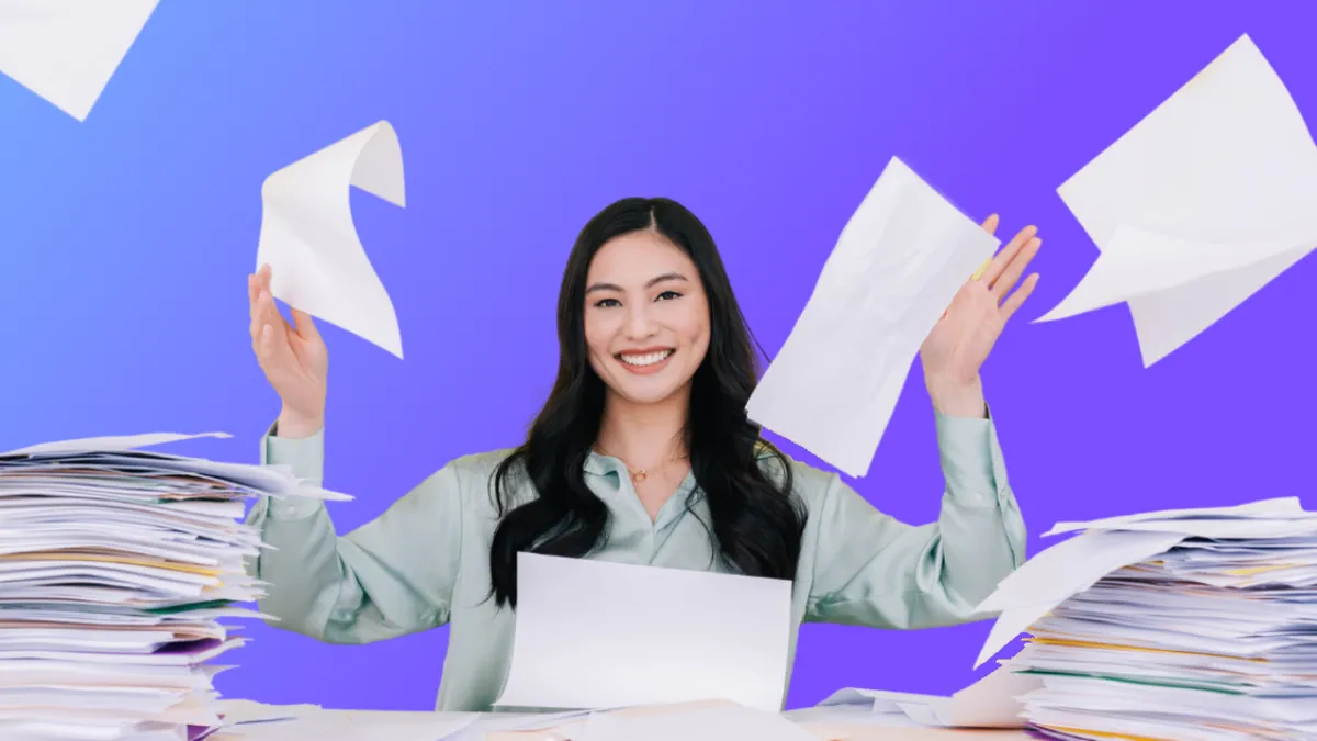 Smiling business person with stacks of papers all over desk and in the air