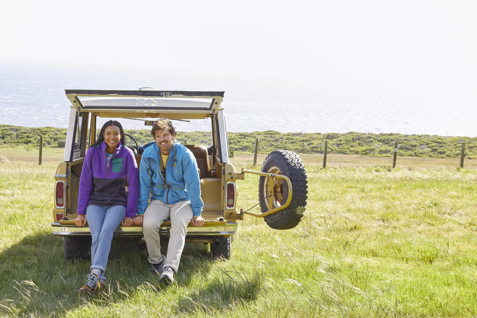 Two people sit in the back of a car with the trunk open.