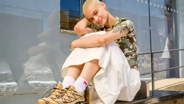 A person hugs their knees on a bench, with Salomon shoes on.